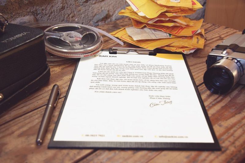 Vintage film reel, an analog movie camera, a fountain pen and a printed letter on a rustic wooden desk