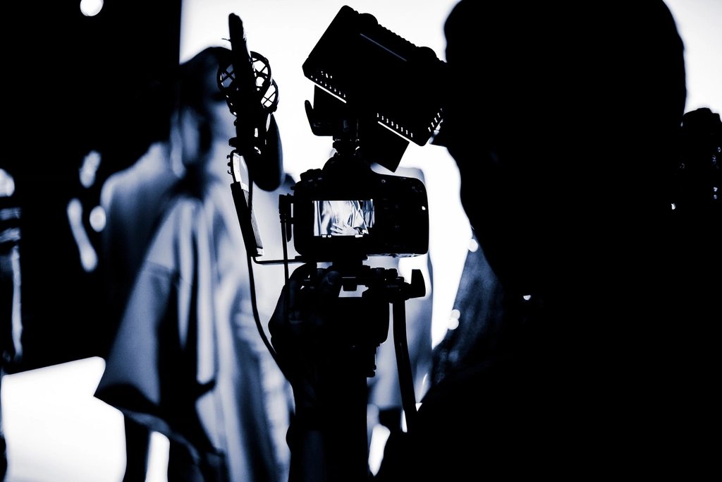Silhouette of a video camera on a tripod with a shotgun microphone and LED light on a studio set, crew in the background