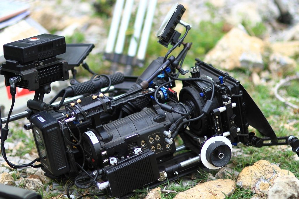 Professional cinema camera rig with follow focus and matte box set on grass at an outdoor video shoot.