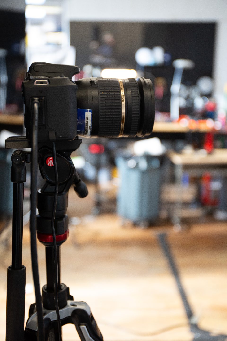 A professional camera with a zoom lens mounted on a tripod in a video production workspace.