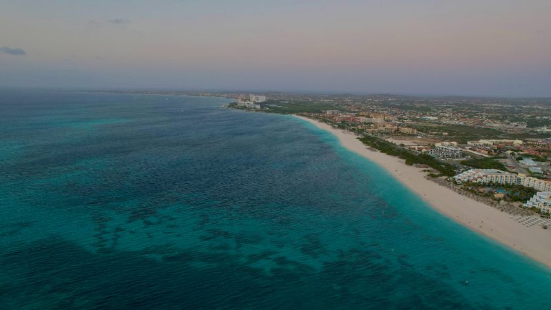 Aerial drone view of a turquoise South Florida coastline with a white sand beach and waterfront buildings at dusk