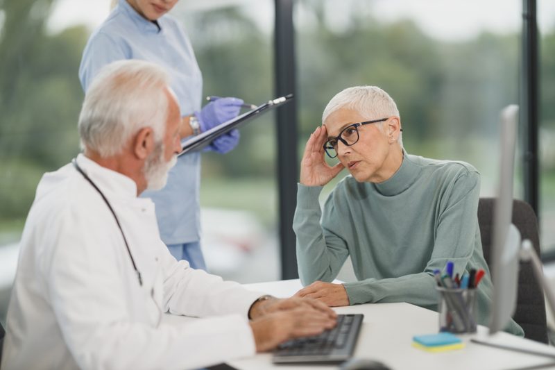 A doctor and a nurse review notes with an older patient during a consultation in a bright medical office