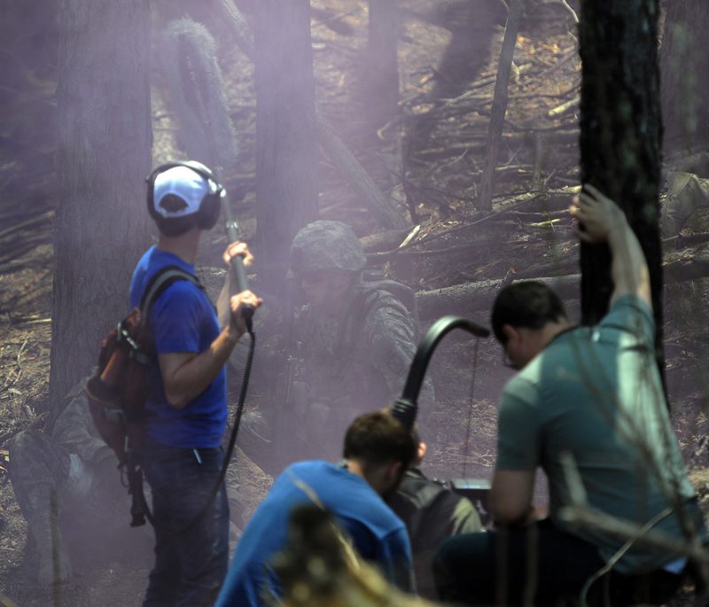 A video production crew on location: a boom mic operator in headphones and a camera operator filming a scene.