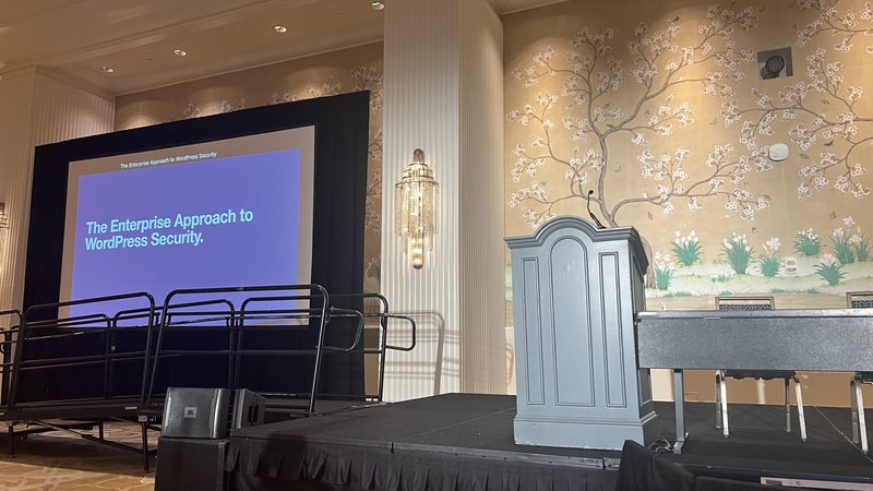 Empty conference ballroom with a stage, podium, microphone and projector screen set up for a corporate event.