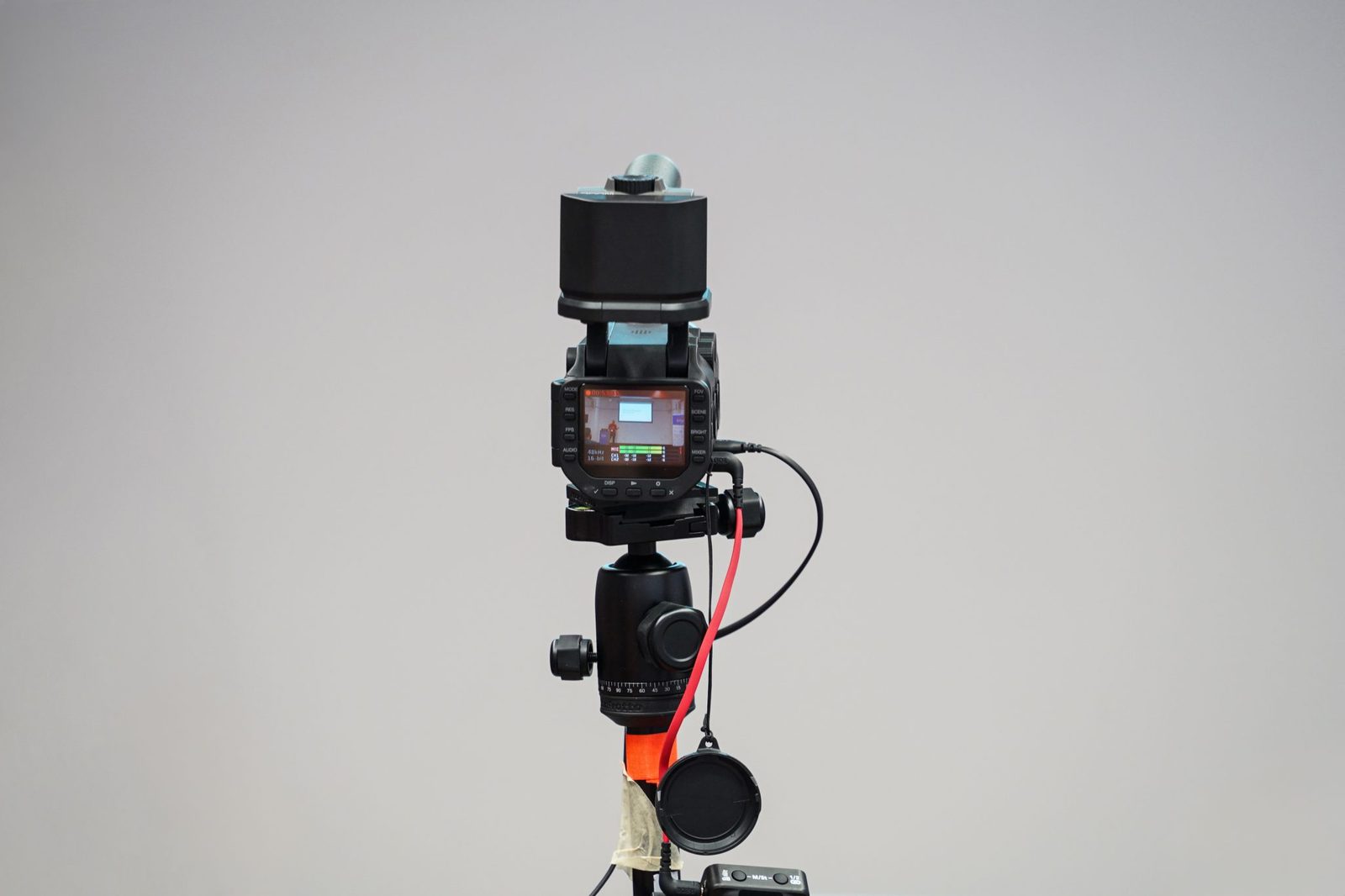 A professional video camera on a tripod with cables connected, its screen showing a live preview of the shot