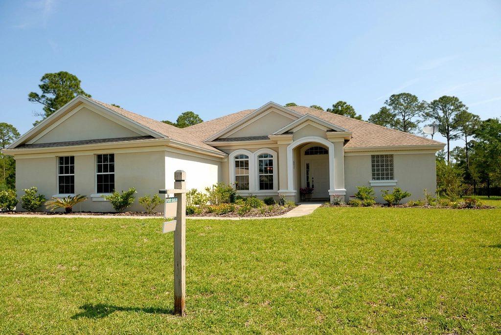 A single-story Florida home with a for-sale sign in the front yard under a clear blue sky.