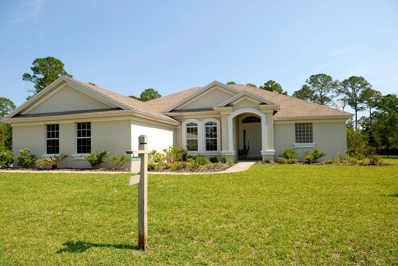 A single-story Florida home with a for-sale sign in the front yard under a clear blue sky.