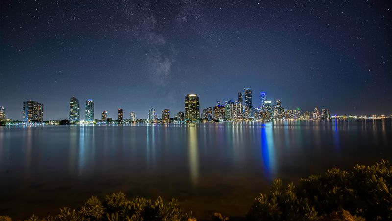 Breathtaking view of Miami's skyline at night with a star-filled sky reflecting over the water.