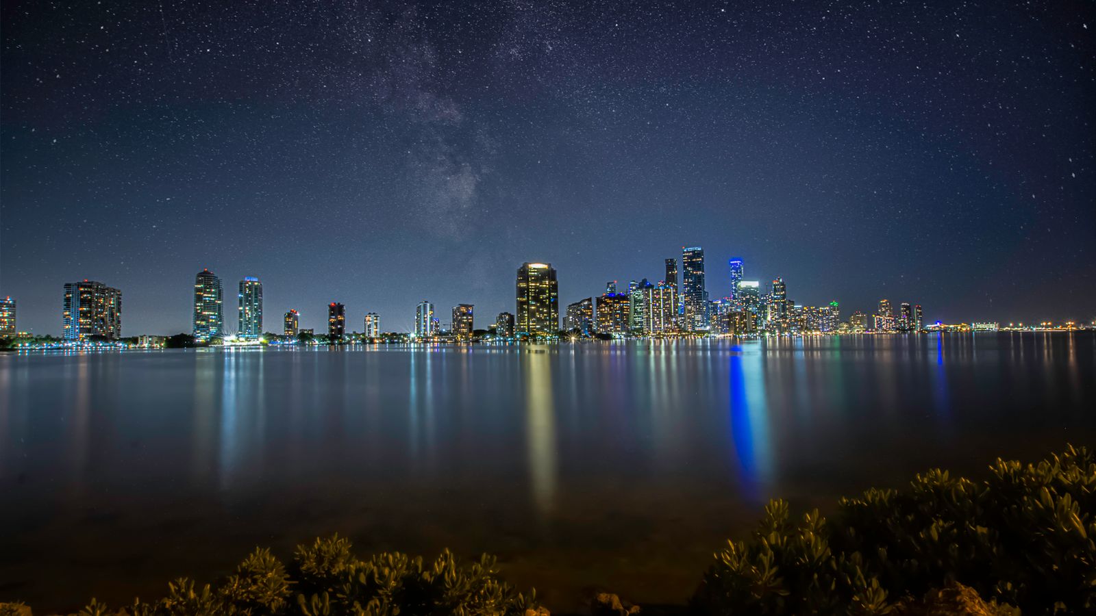Breathtaking view of Miami's skyline at night with a star-filled sky reflecting over the water.