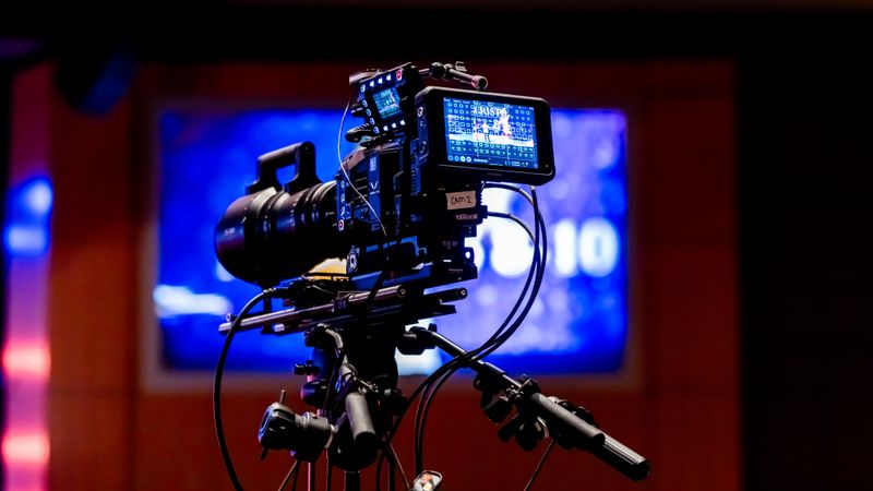Professional cinema camera on a tripod on a studio set under blue stage lighting.