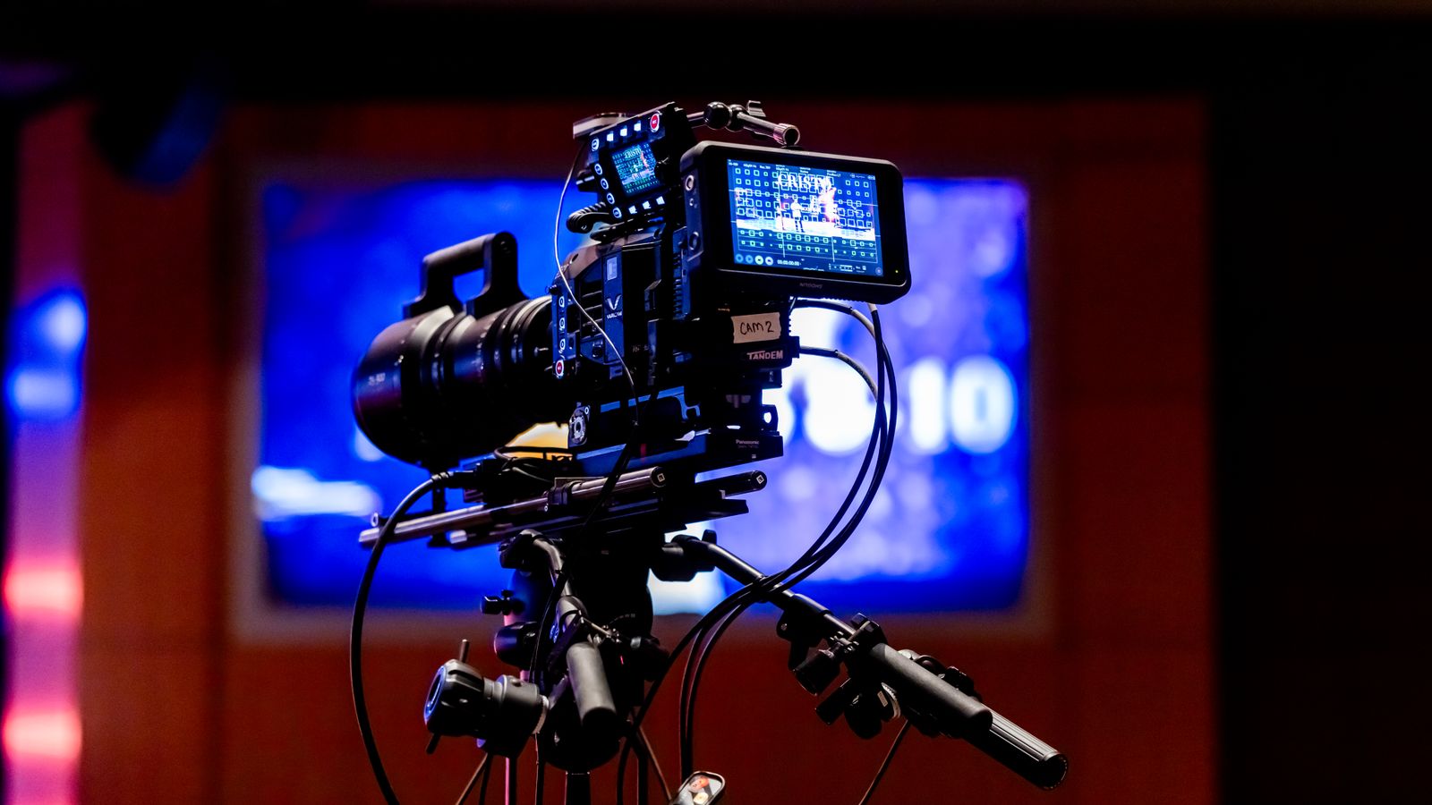 Professional cinema camera on a tripod on a studio set under blue stage lighting.
