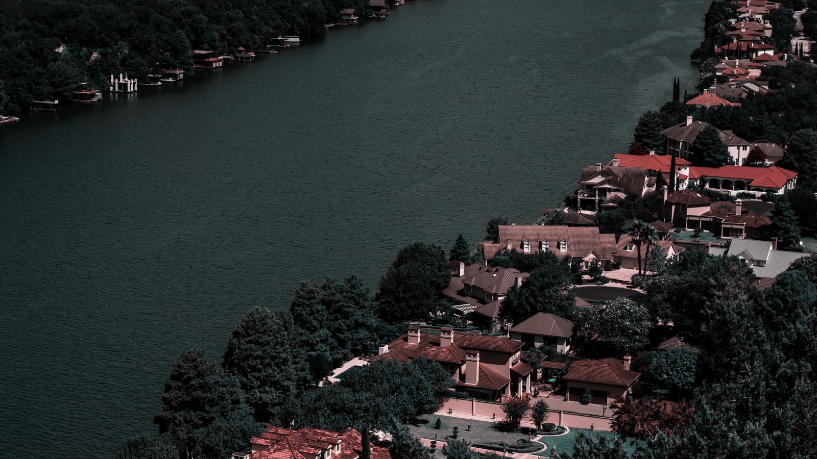 Aerial view of elegant homes along a tranquil river surrounded by lush greenery, showcasing affluence and scenic beauty.