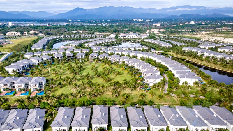Aerial view of modern residential community with green spaces, palm trees, and blue pools.