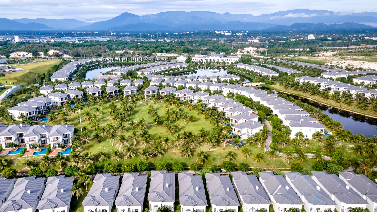 Aerial view of modern residential community with green spaces, palm trees, and blue pools.