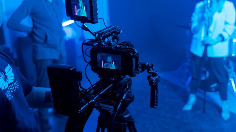 Behind the scenes of a music video recording with professional film equipment and studio lighting.
