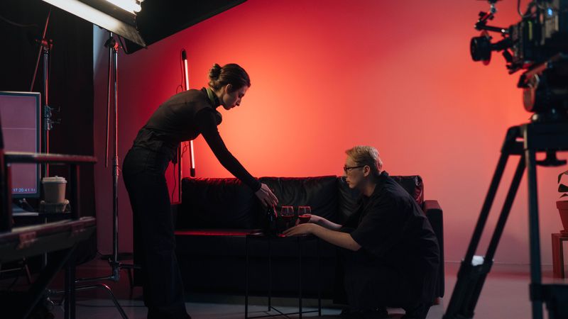 Behind-the-scenes view of a film crew in action, setting up a studio scene with lighting and equipment.