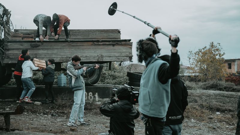 Film crew working outdoors, capturing scenes with camera and boom mic.