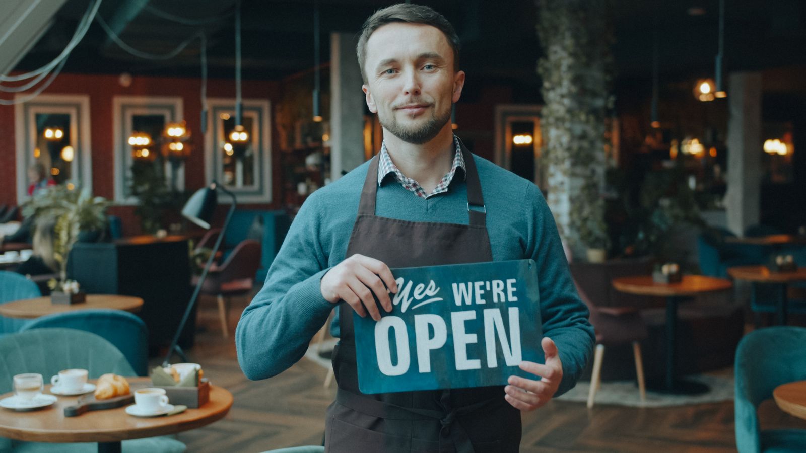 Cafe owner holding a We're Open sign inside his restaurant