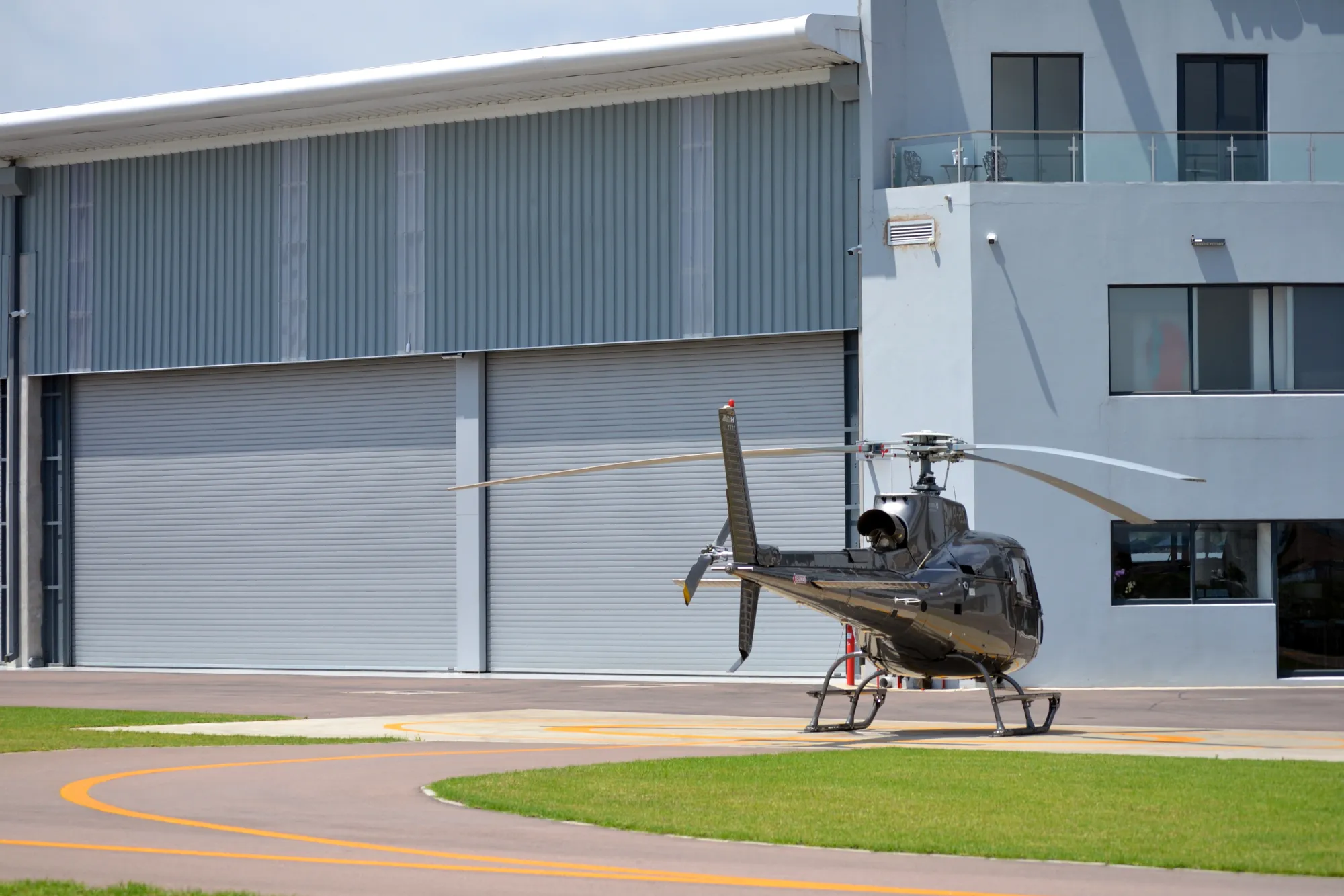 Black helicopter parked on a helipad near a building with large closed industrial doors.