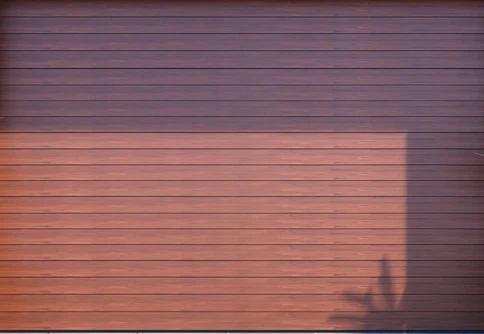 Brown horizontal wooden panel garage door with a shadow of a plant on the lower right side.