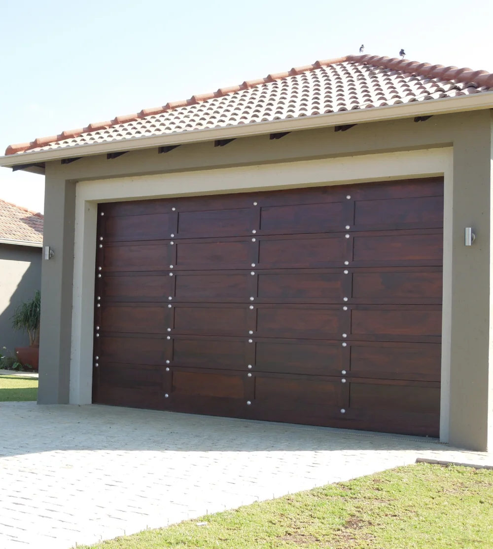 Modern house with a closed dark wooden garage door and a tiled roof under clear sky.