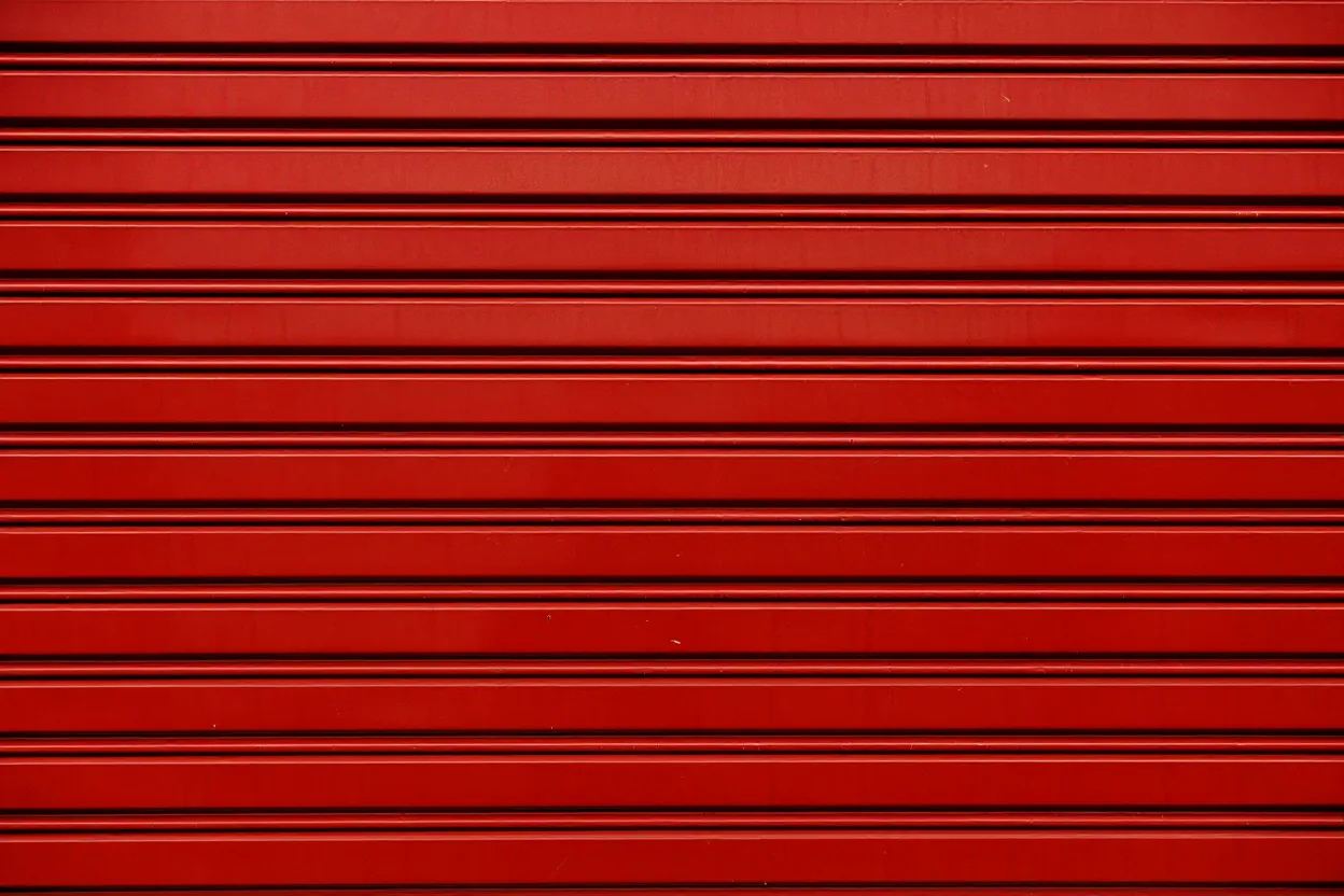 Close-up of a red metal roll-up shutter door with horizontal slats.