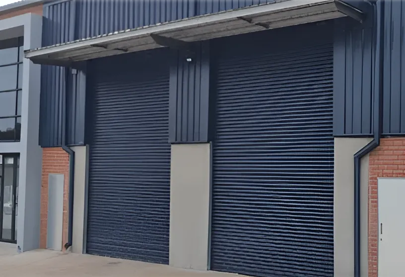 Two closed dark blue industrial rolling shutter doors on a building with a concrete driveway.