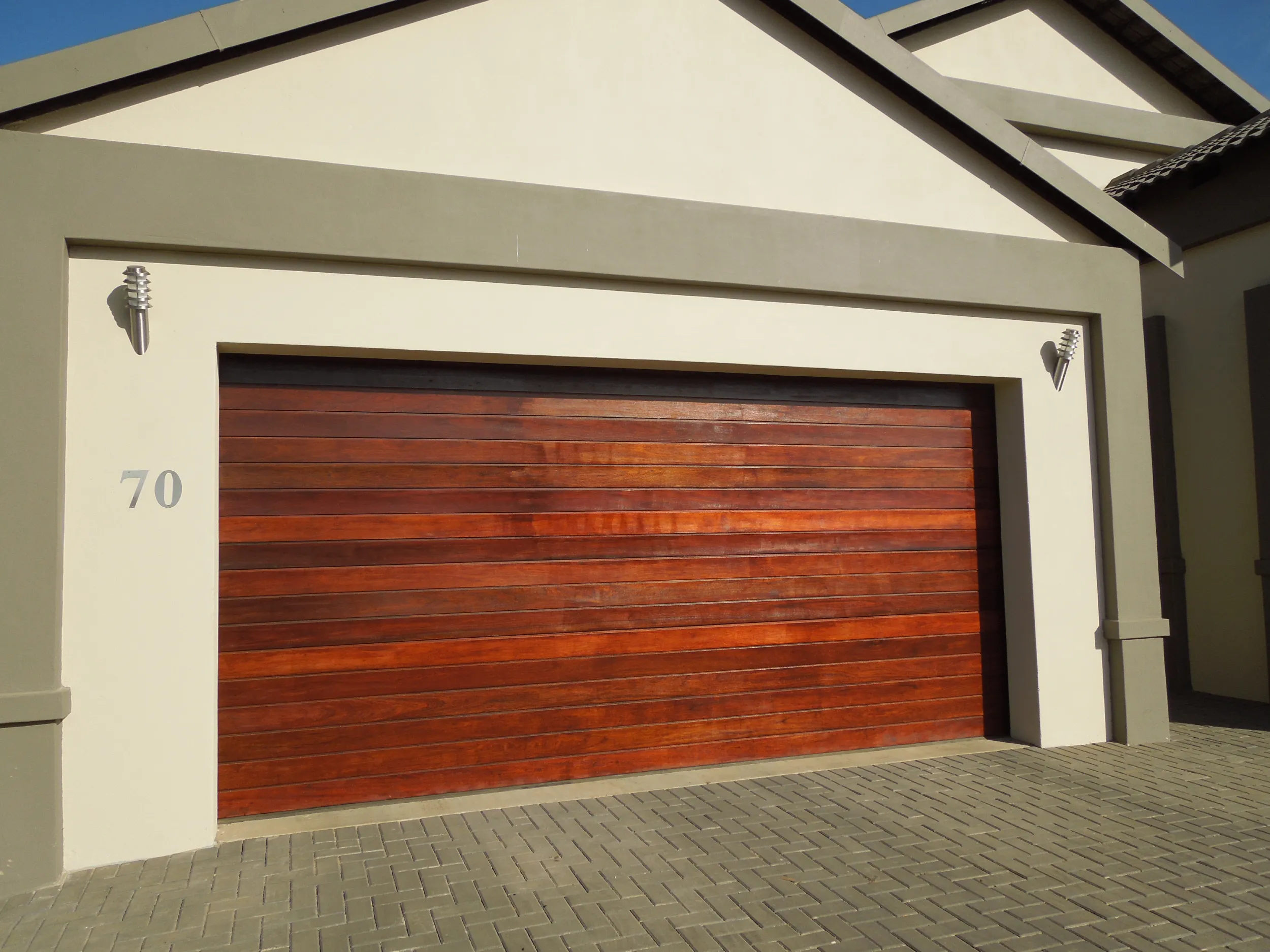 Modern house garage with horizontal wooden slatted door and house number 70 on cream and beige exterior.