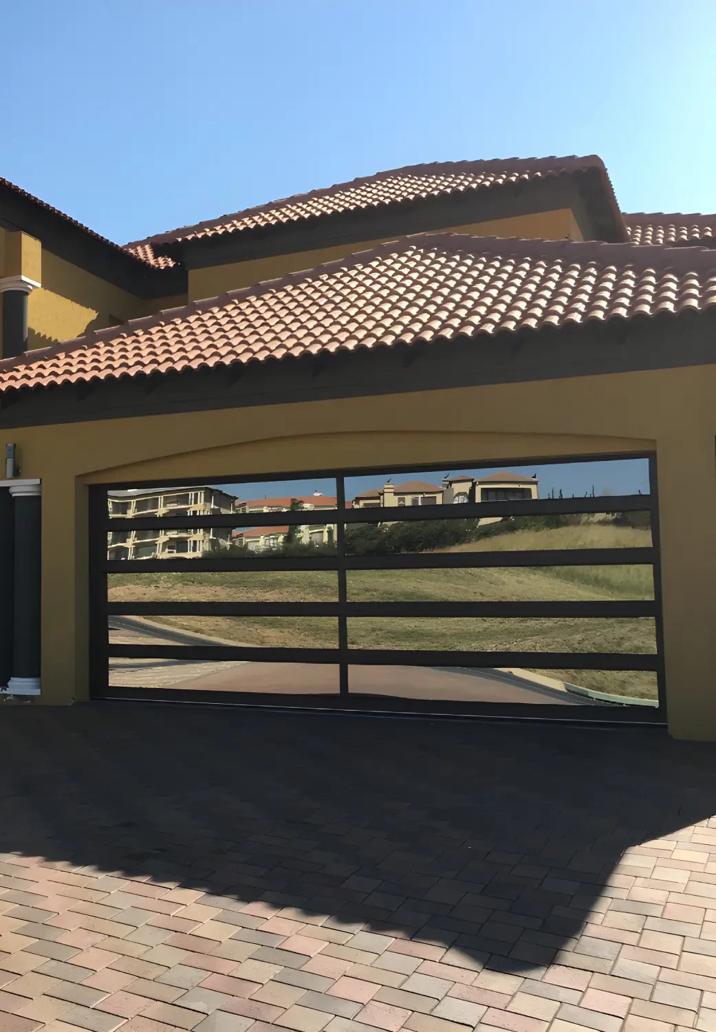 Modern house with a yellow exterior and a large garage door that has horizontal black frames and reflective glass panels.