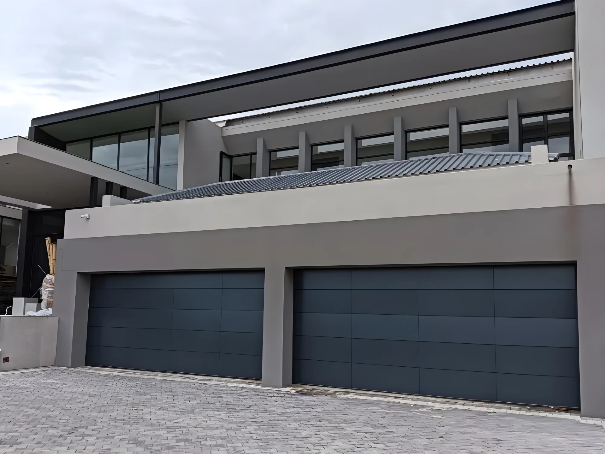 Modern house exterior with a flat roof, large windows, and two closed dark gray garage doors.