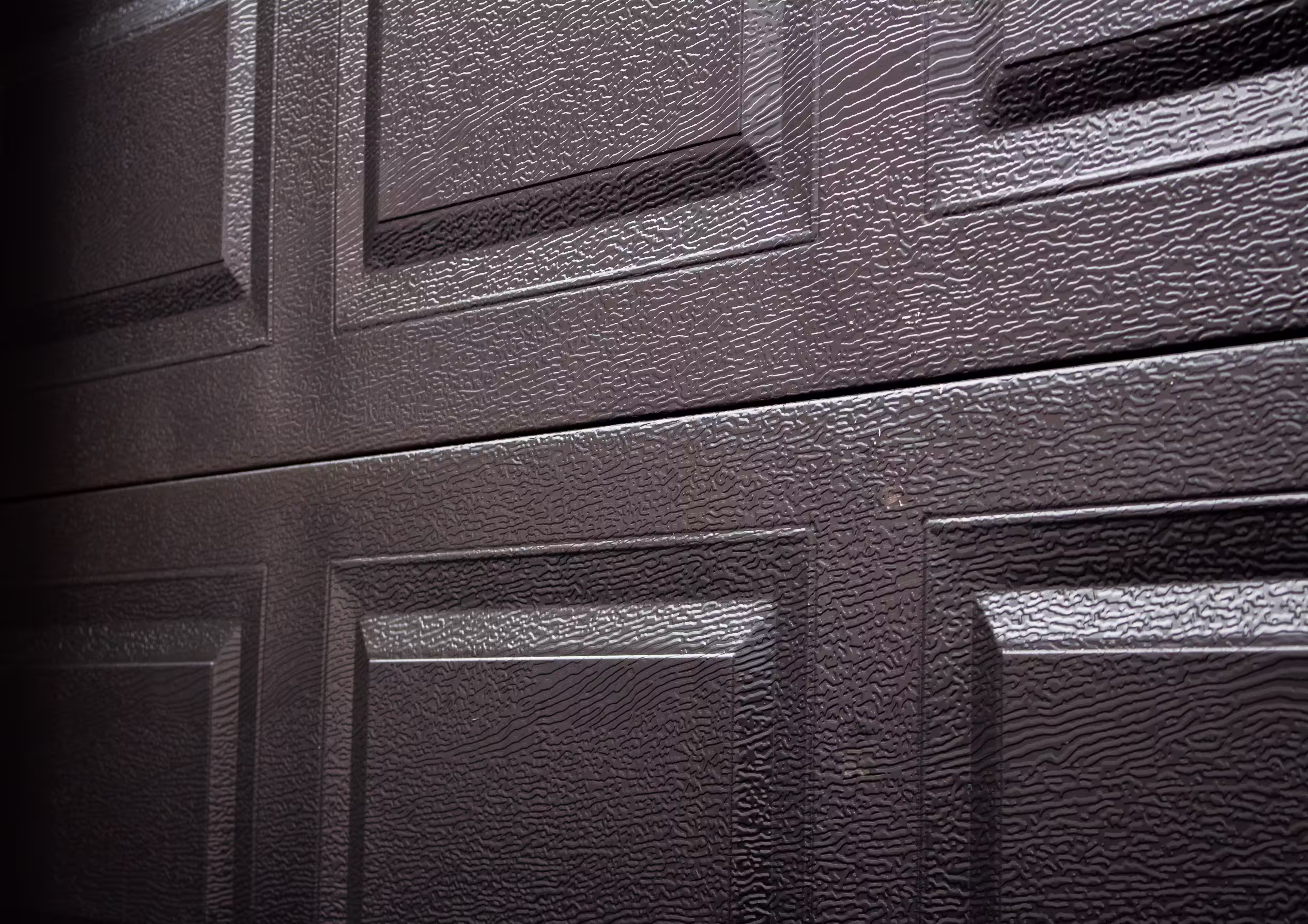 Close-up of a textured dark brown steel garage door with raised rectangular panels.