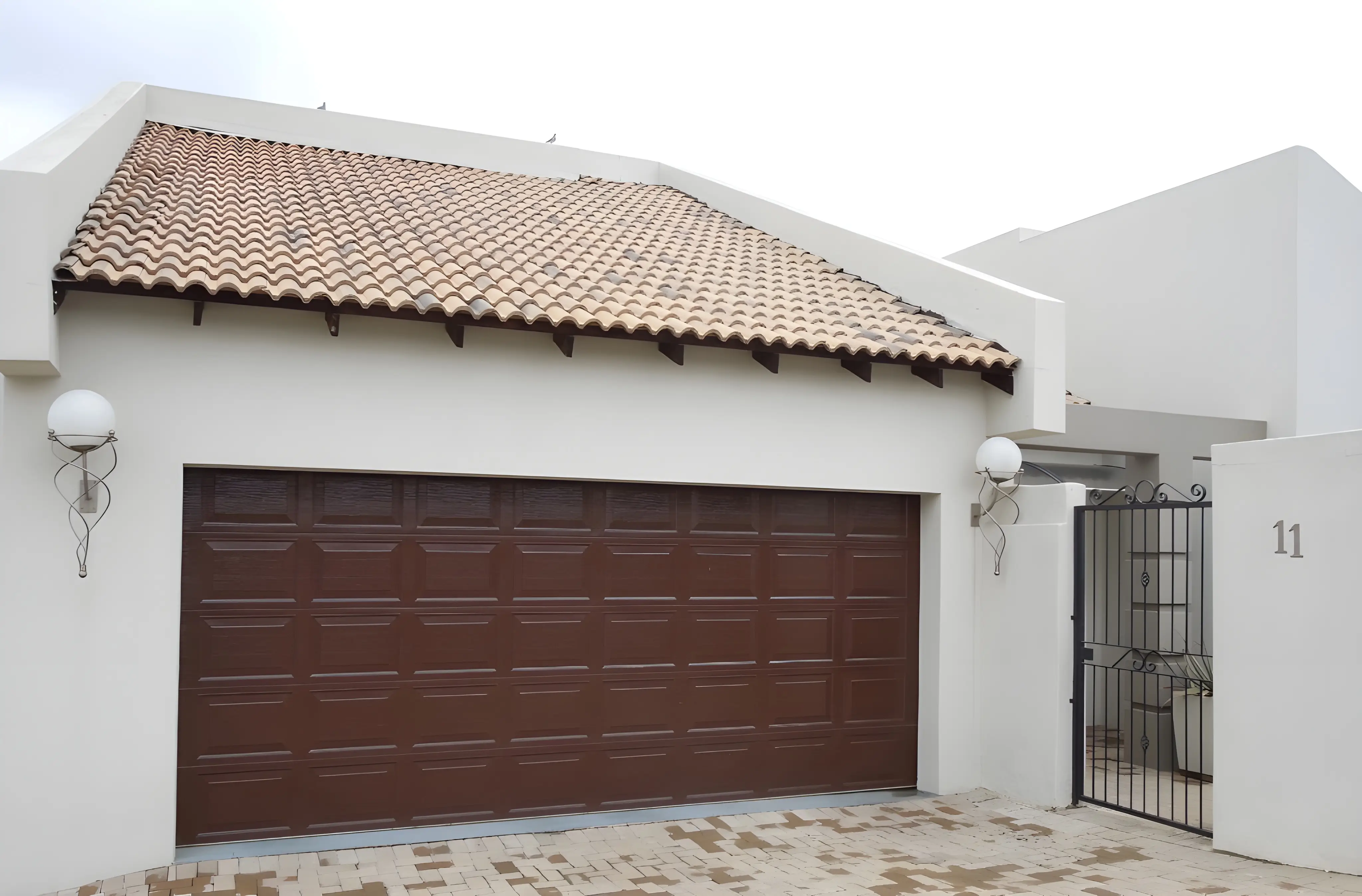 Modern white house exterior with a terracotta tiled roof, brown sectional garage door, and black wrought iron gate numbered 11.