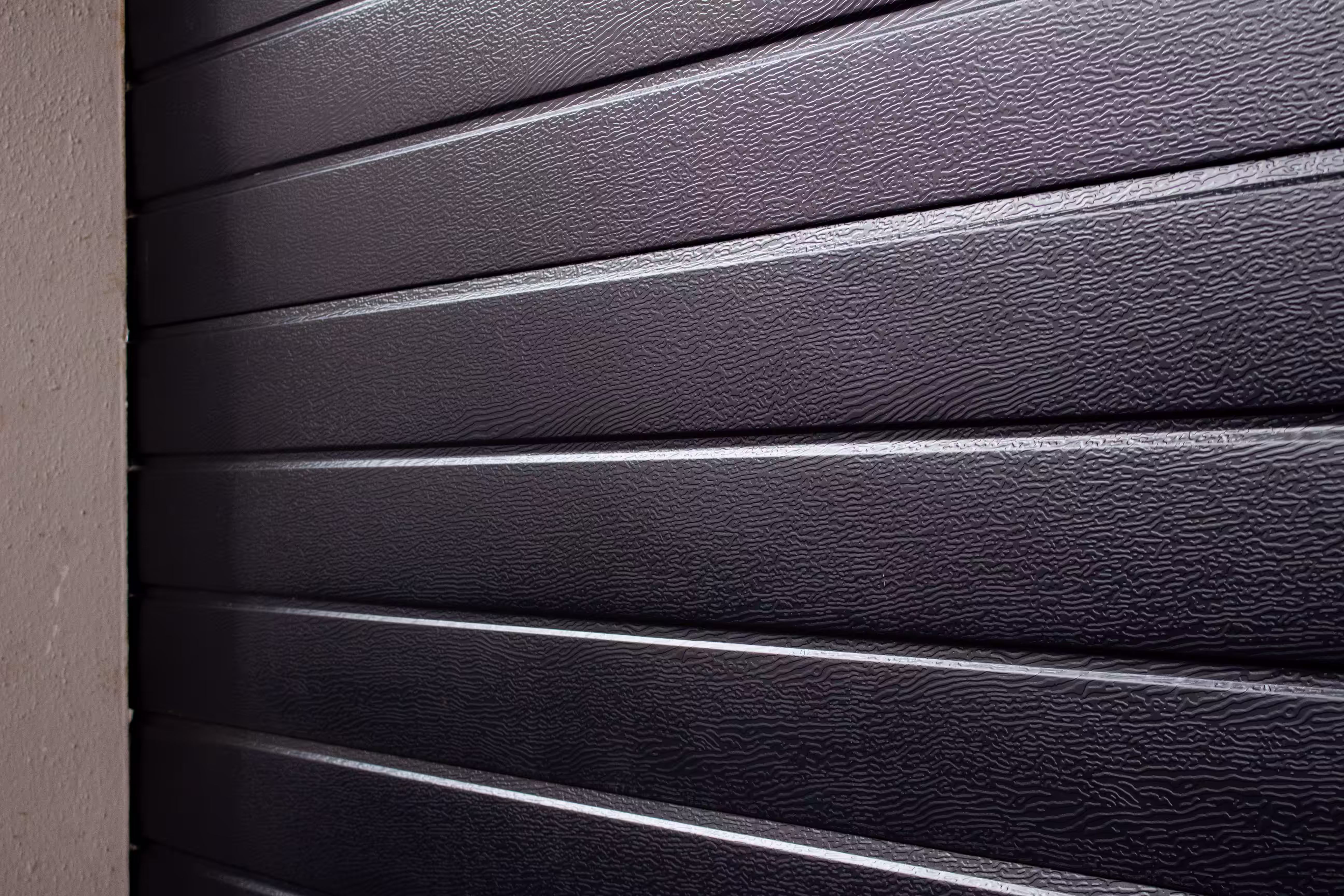 Close-up of black horizontal steel garage door panels with textured surface next to a beige wall.