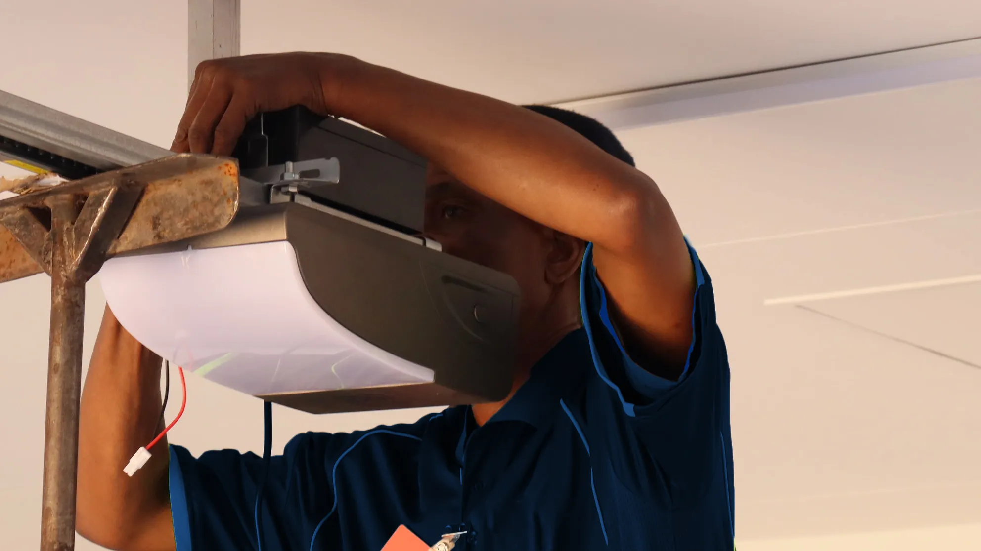Technician installing or repairing a garage door opener mounted on a ceiling.