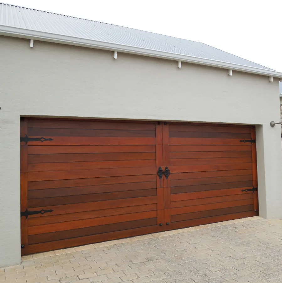 Double wooden garage doors with horizontal panels and black decorative hinges on a light gray building.