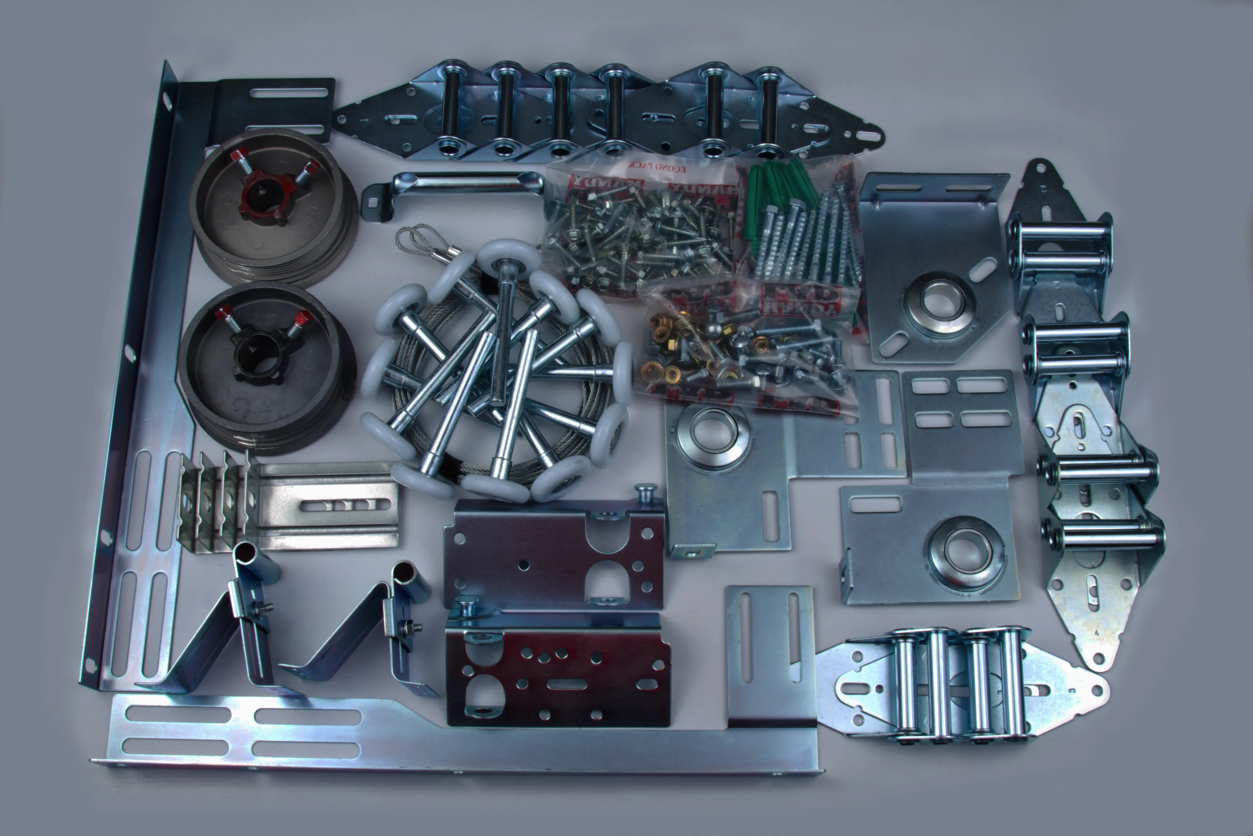 Collection of metal spare parts including brackets, rollers, screws, pulleys, and fasteners arranged on a flat surface.