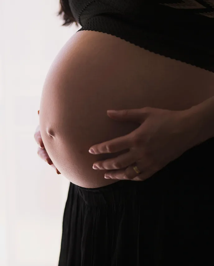 A pregnant woman in a black dress holding her belly.