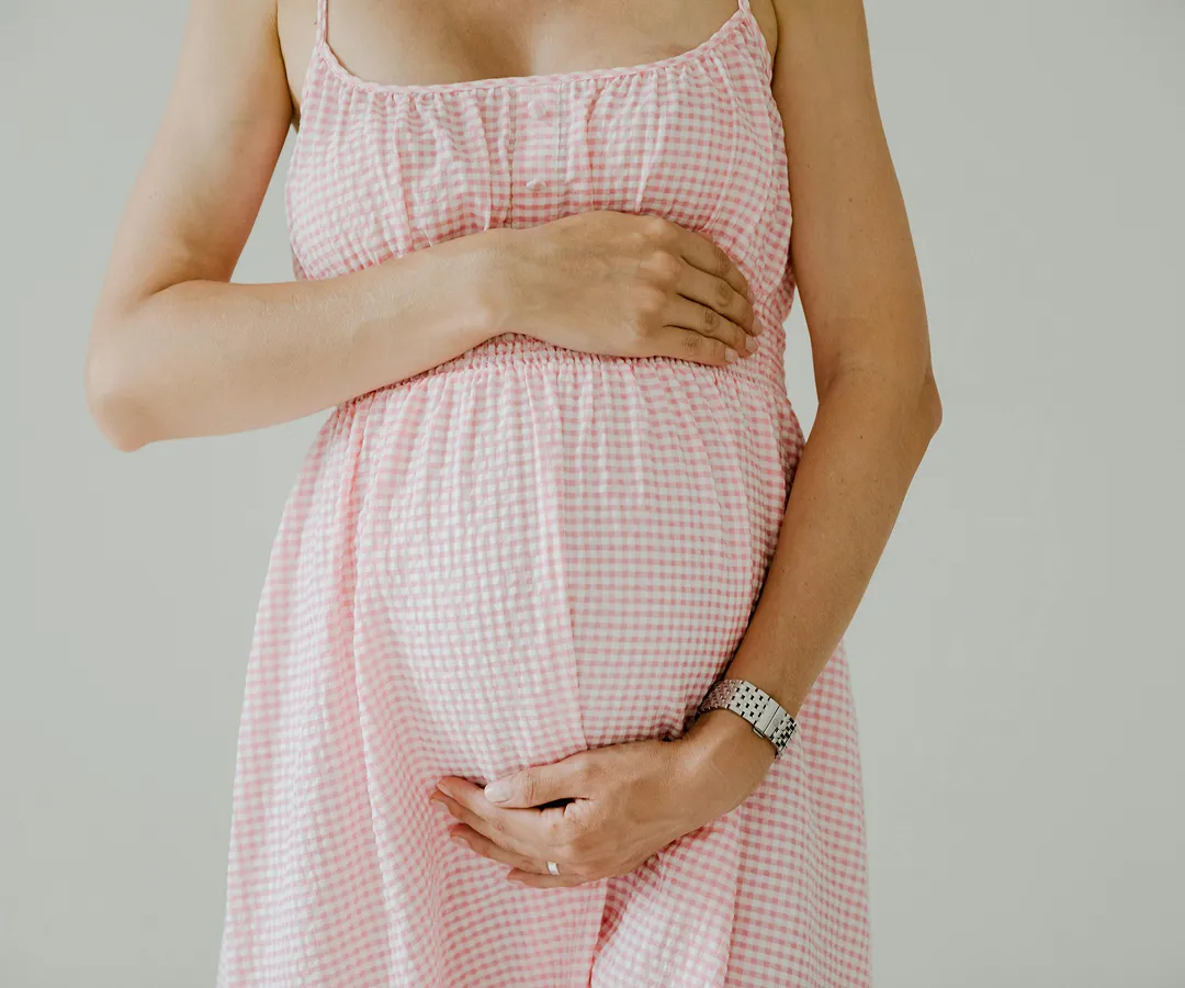 A pregnant woman in a pink dress holding her stomach.