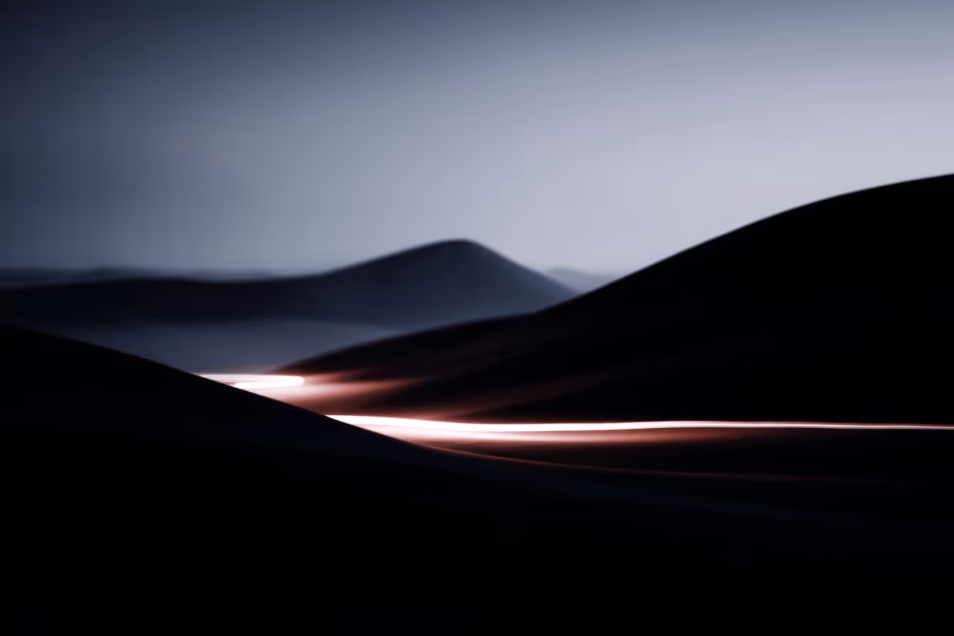 Dark hills with streaks of bright light cutting across the landscape under a blue-gray sky.