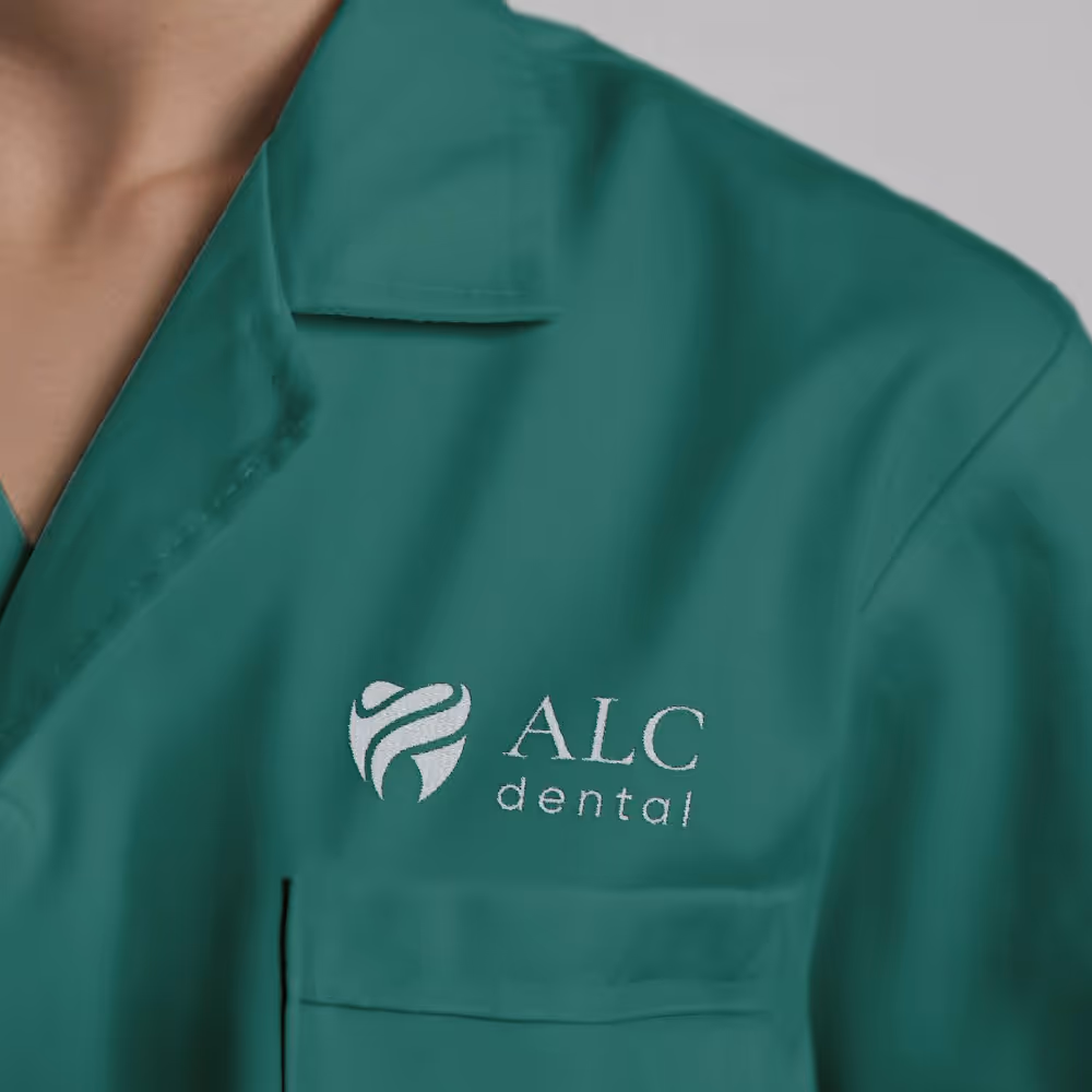 Close-up of green medical scrubs with ALC Dental logo embroidered on the chest pocket.