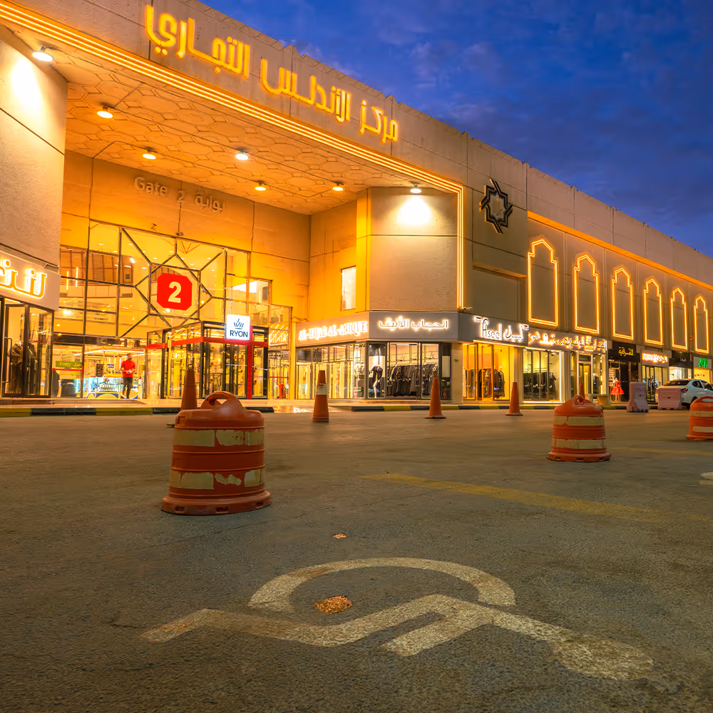 Exterior view of Andalus Mall entrance illuminated at dusk with Arabic signage and visible handicap parking symbol on the ground.