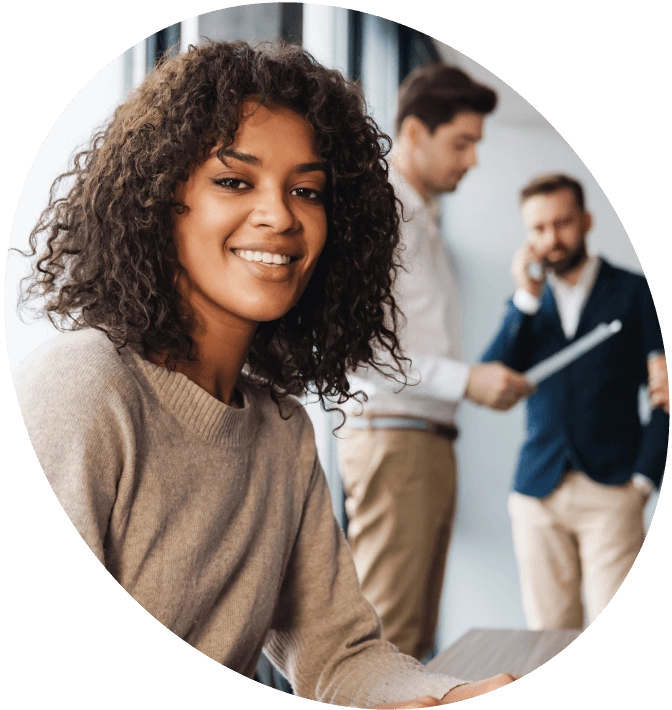 Smiling woman in an office setting with colleagues in the background.