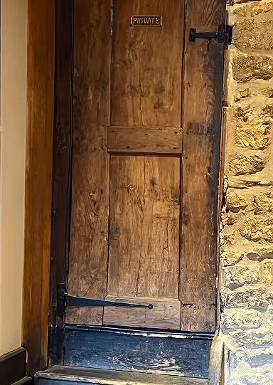 Old wooden door with a 'PRIVATE' sign, set in a stone wall with metal hinges and latch.
