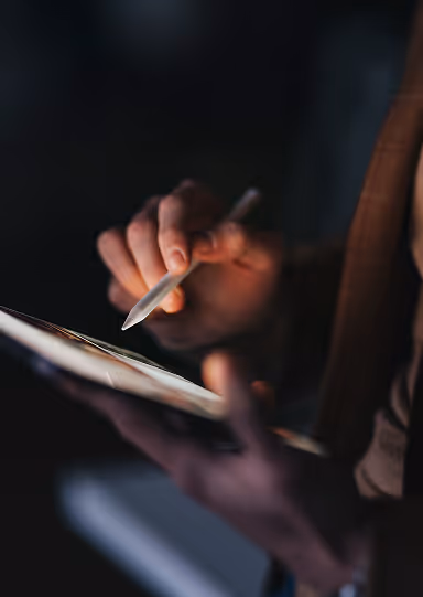 Person using a stylus to write on a digital tablet in low light.