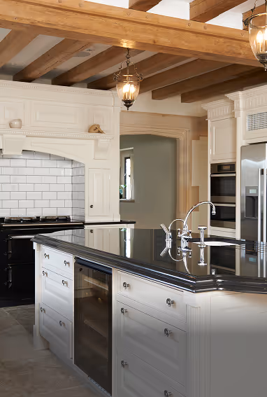 Modern kitchen with white cabinetry, black countertop island with built-in wine cooler, stainless steel appliances, and exposed wooden ceiling beams.