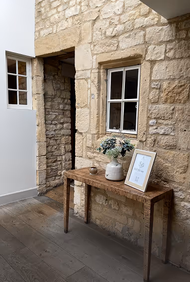Rustic stone wall with white-framed window and wooden console table holding a vase with greenery and a framed print.