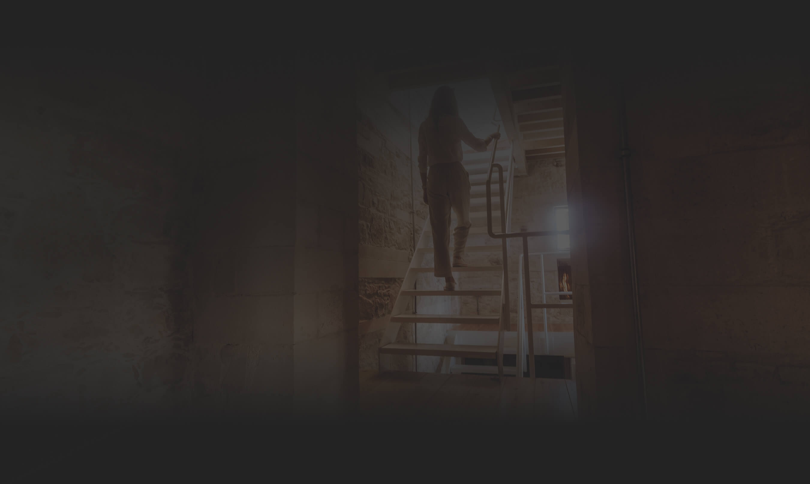 Person ascending a modern metal staircase inside a stone-walled building with natural light from a window.