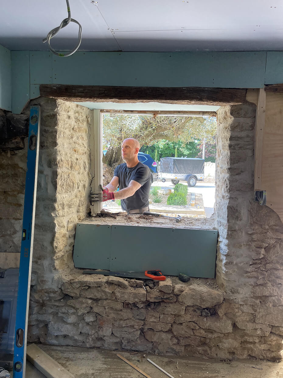 Man wearing gloves working on installing a window frame in a stone wall during construction or renovation.