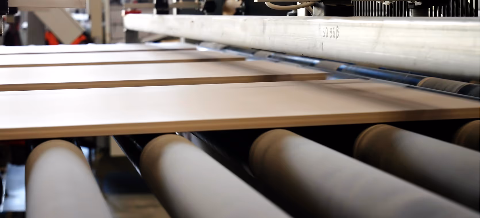 Wood panels moving on conveyor rollers in a manufacturing facility.