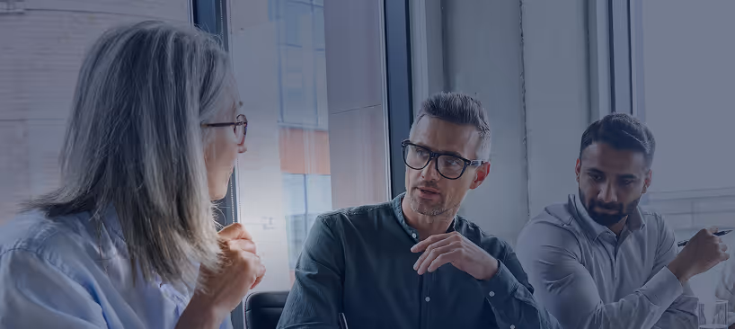 Three colleagues engaged in a serious discussion in a modern office with large windows.